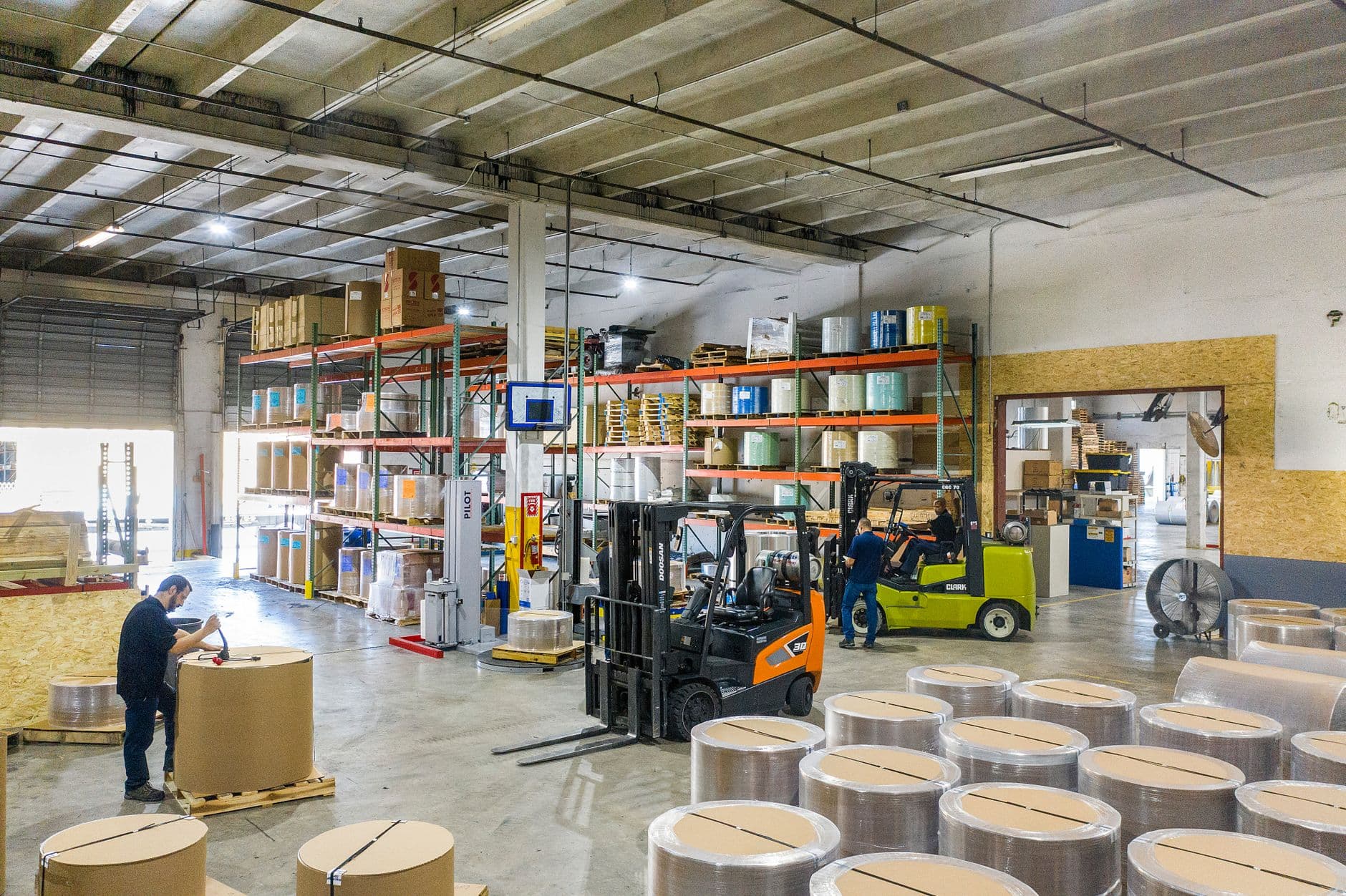 Warehouse operatives wrapping and moving palletised goods with forklifts